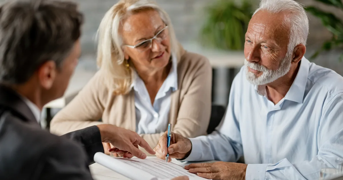 Casal maduro em reunião com consultor assinando documentos de planejamento sucessório familiar